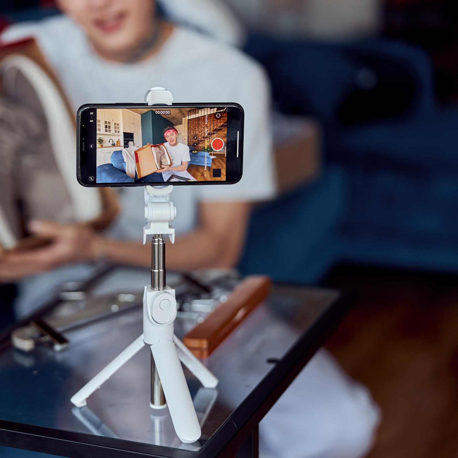 An image of a phone on a tripod, capturing a video of a man holding a pair of shoes